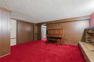 Carpeted bedroom with wood walls, a brick fireplace, a textured ceiling, and a closet
