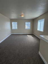 Unfurnished room with dark carpet, plenty of natural light, and a textured ceiling