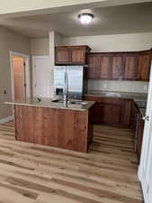 Kitchen with a kitchen island with sink, stainless steel refrigerator with ice dispenser, dark stone counters, electric range, and light wood-type flooring
