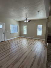 Unfurnished living room with light wood-style flooring, a textured ceiling, and a ceiling fan