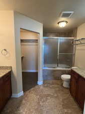 Bathroom featuring vanity, a walk in closet, a textured ceiling, and combined bath / shower with glass door