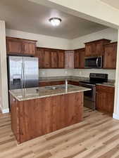 Kitchen featuring stainless steel appliances, light stone countertops, a kitchen island with sink, light wood-style floors, and a textured ceiling