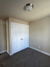 Unfurnished bedroom featuring a textured ceiling, dark carpet, and a closet