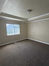Unfurnished room featuring dark carpet, ornamental molding, and a textured ceiling