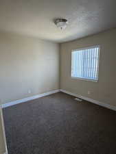 Empty room with dark carpet and a textured ceiling