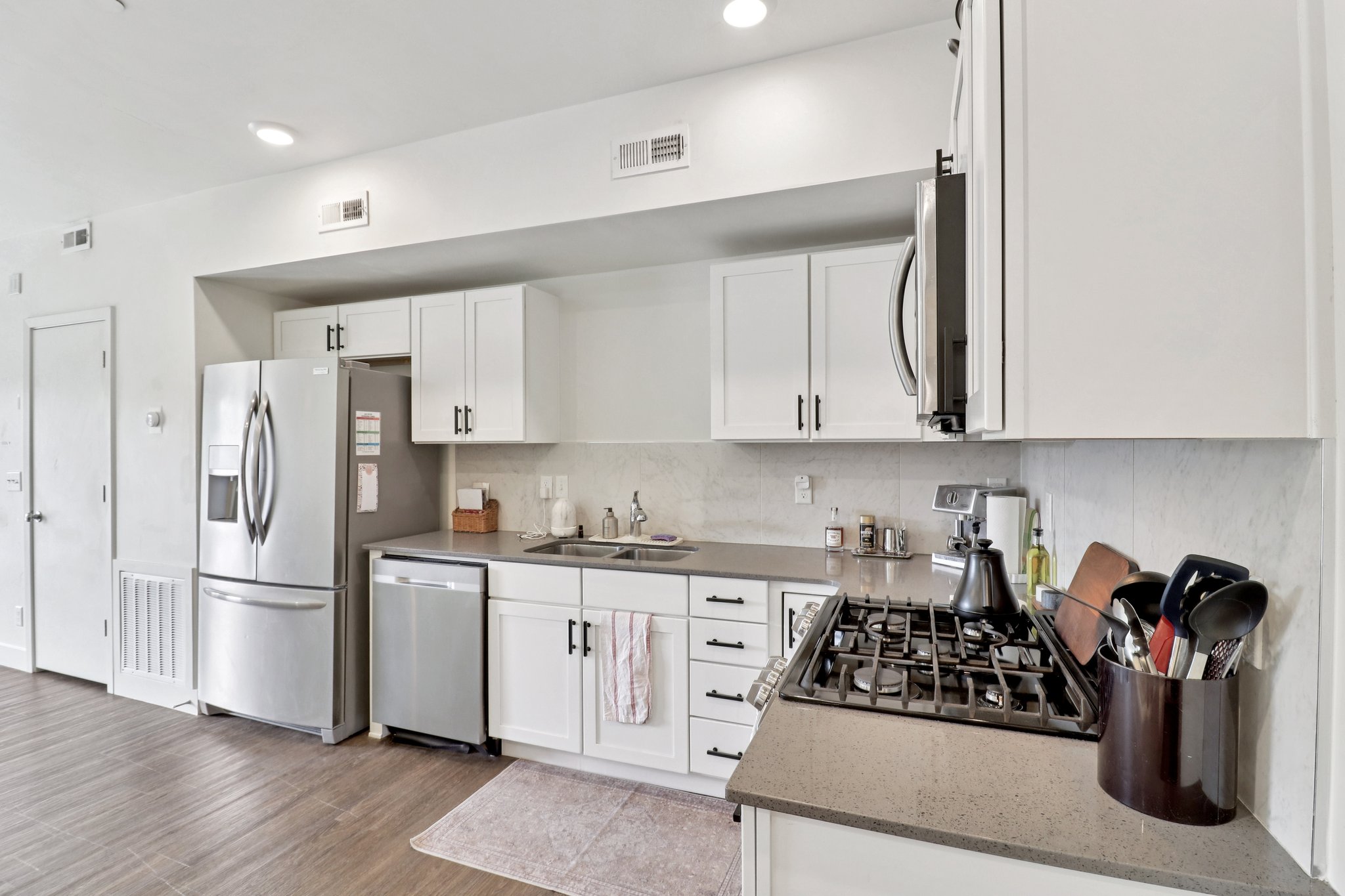 Kitchen with white cabinets, light stone counters, stainless steel appliances, light wood-style floors, and tasteful backsplash