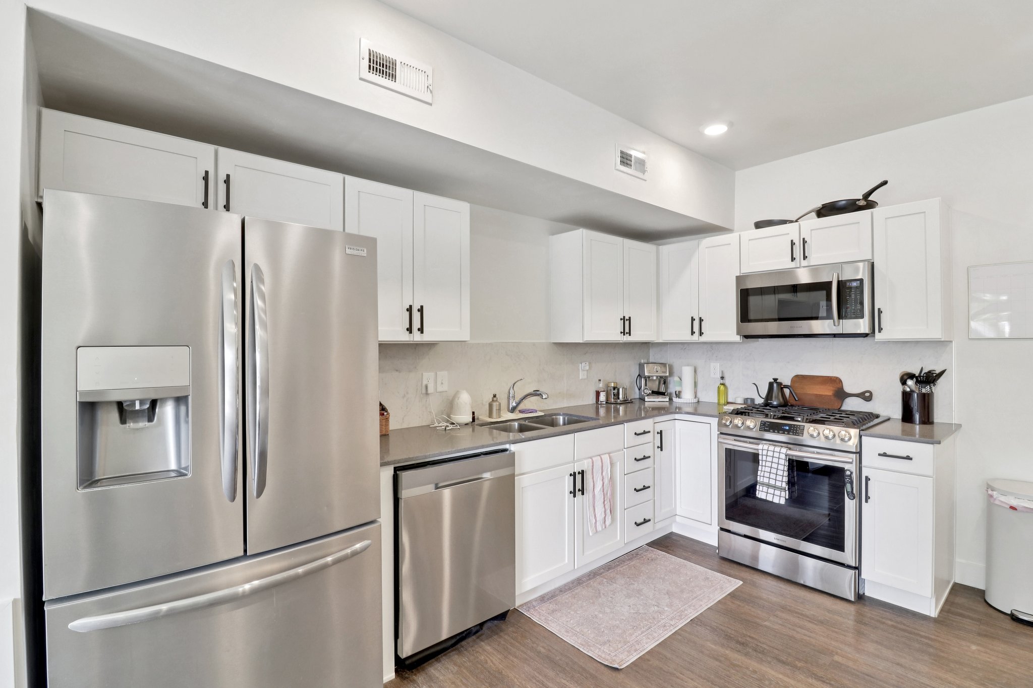 Kitchen with stainless steel appliances, white cabinetry, dark wood-type flooring, and dark stone counters