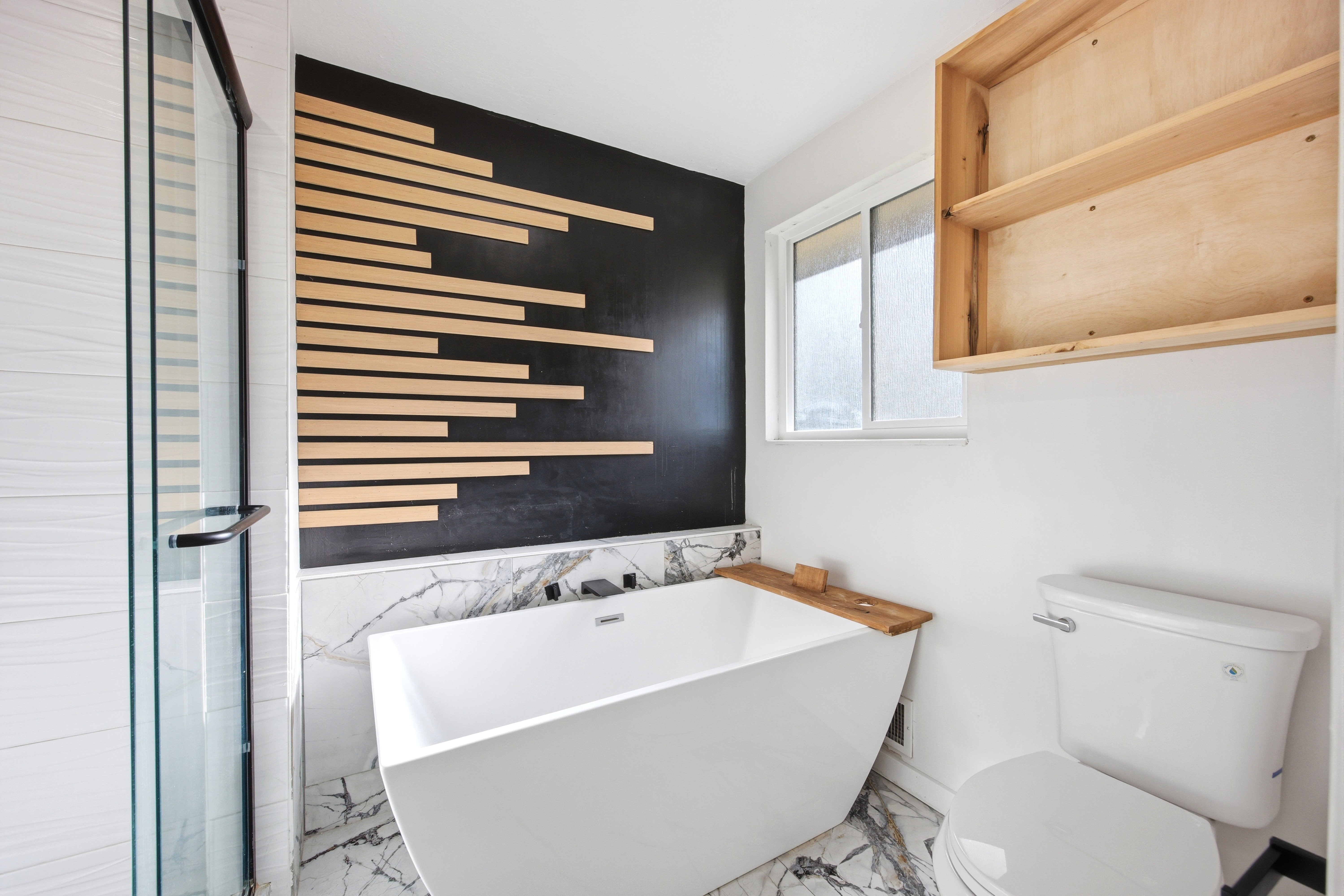 Modern bathroom featuring a freestanding soaking tub, marble-look tile flooring and wainscoting, and a glass-enclosed shower with white tiled walls