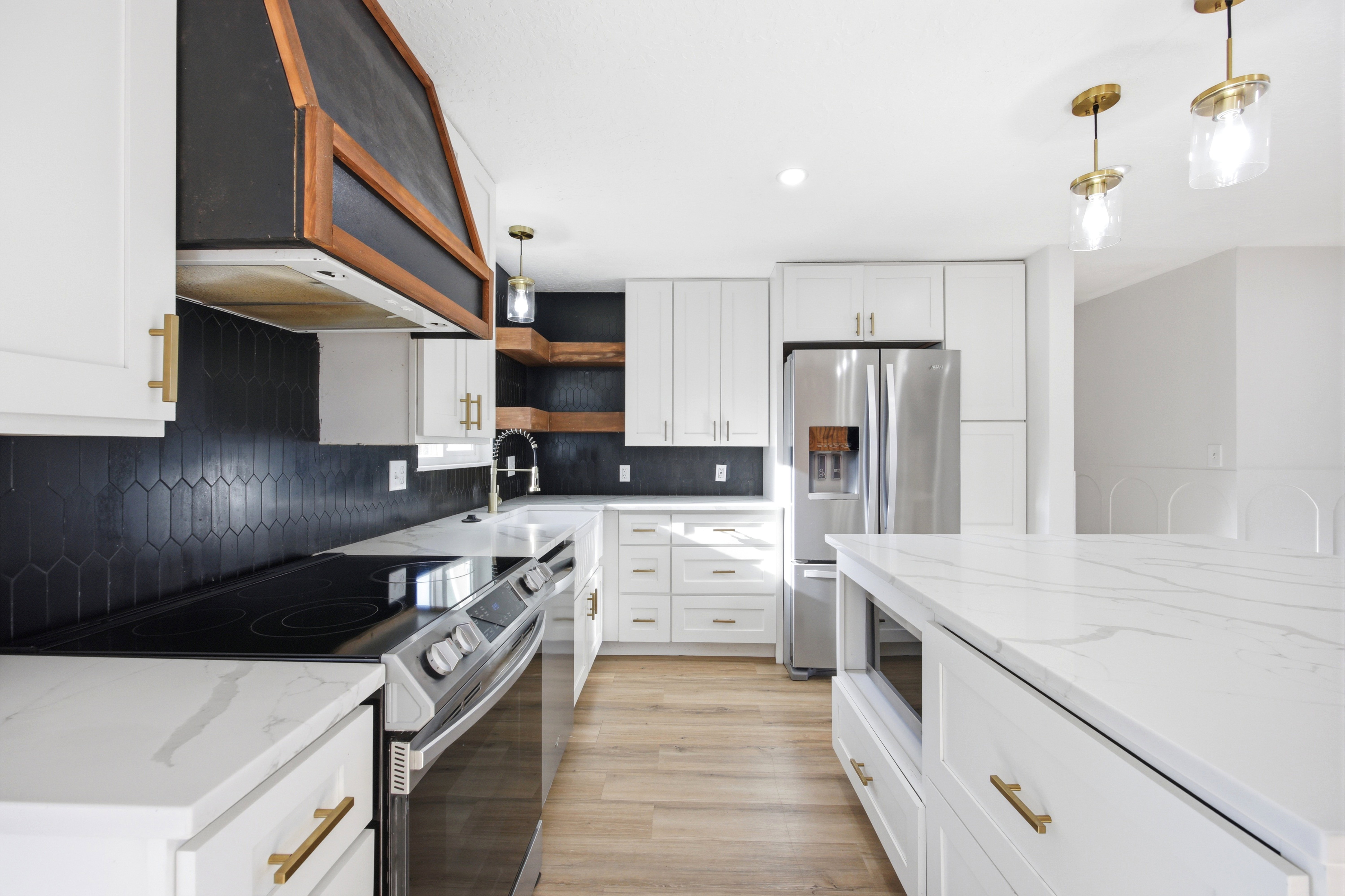 Modern kitchen featuring white cabinetry, quartz countertops, a black picket tile backsplash, and stainless steel appliances