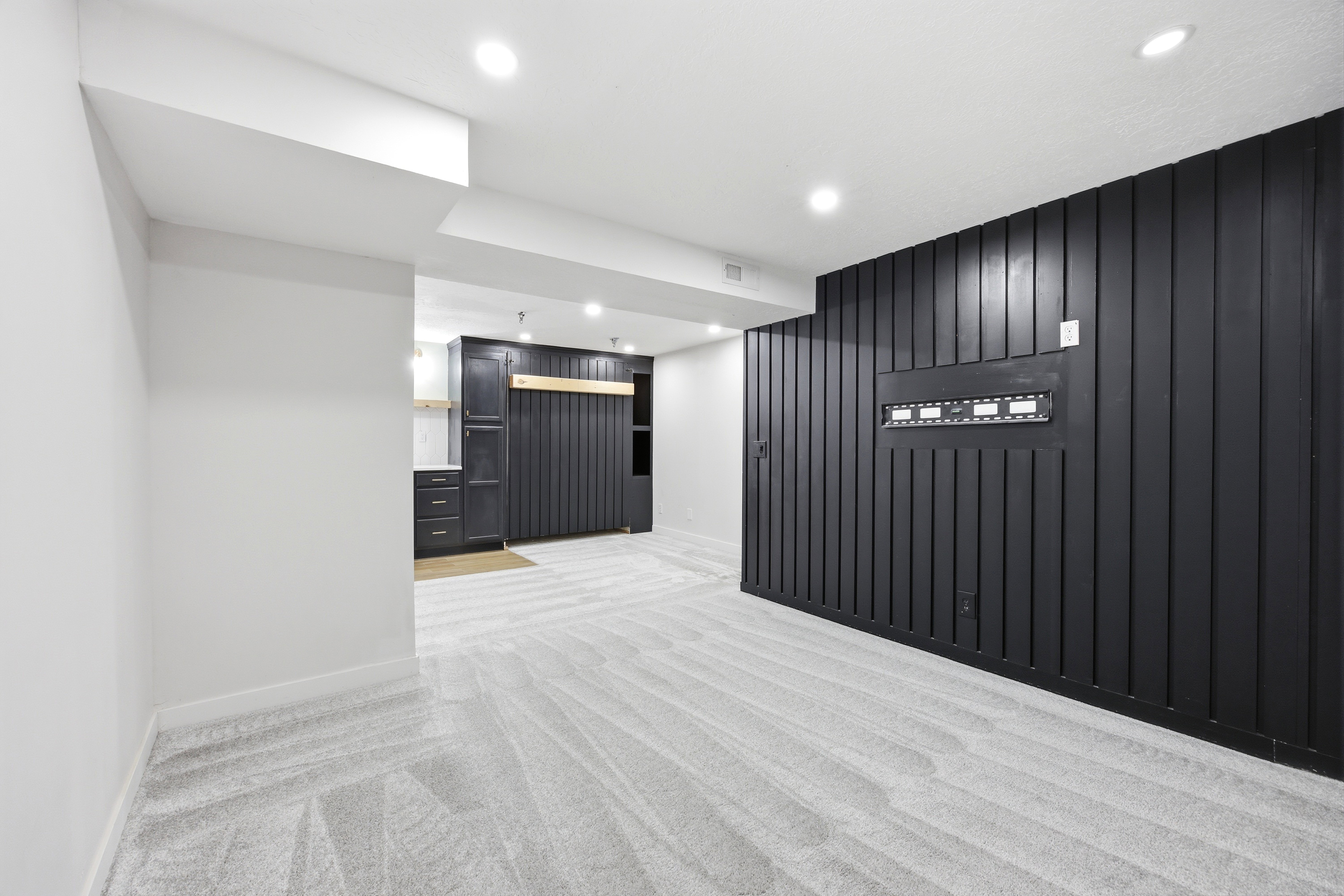 Contemporary living area featuring patterned carpet, recessed lighting, and a striking black accent wall with vertical paneling
