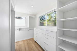 Custom closet system featuring wood-finish flooring, recessed lighting, built-in shelving, integrated drawers with metal hardware, and natural light from horizontal windows
