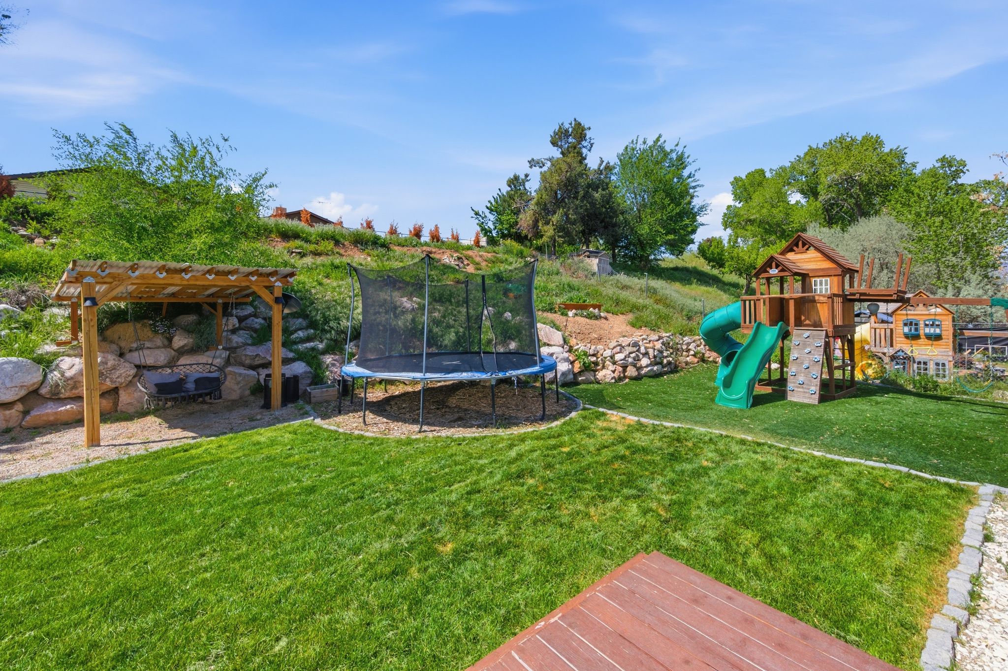 View of grassy yard with a trampoline, a playground, and a pergola