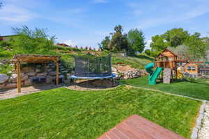 View of grassy yard with a trampoline, a playground, and a pergola