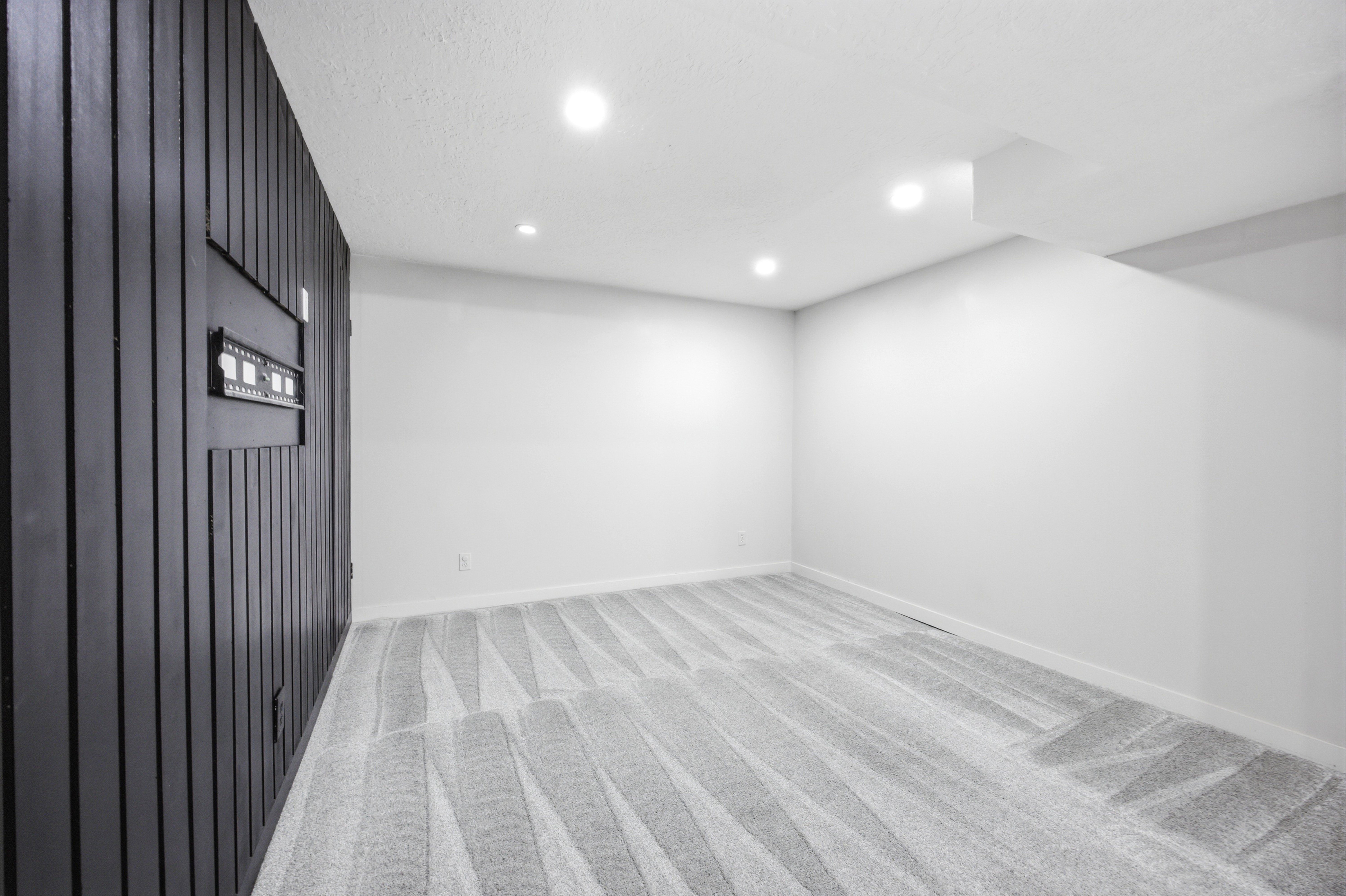 Recessed lighting illuminates a spacious room featuring a distinctive black paneled accent wall
