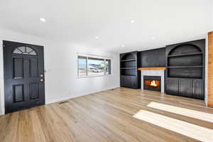 Living area featuring wood-finish flooring, recessed lighting, and a prominent fireplace with a light-toned mantel