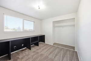 Room featuring a large window with blinds, a built-in dark storage and desk unit, wall-to-wall carpeting, and an open closet with a hanging rod