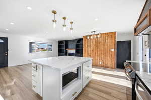 Open-concept living space featuring a white kitchen island with a quartz countertop, recessed lighting, wood-finish flooring, a wood accent wall, and built-in shelving with a fireplace