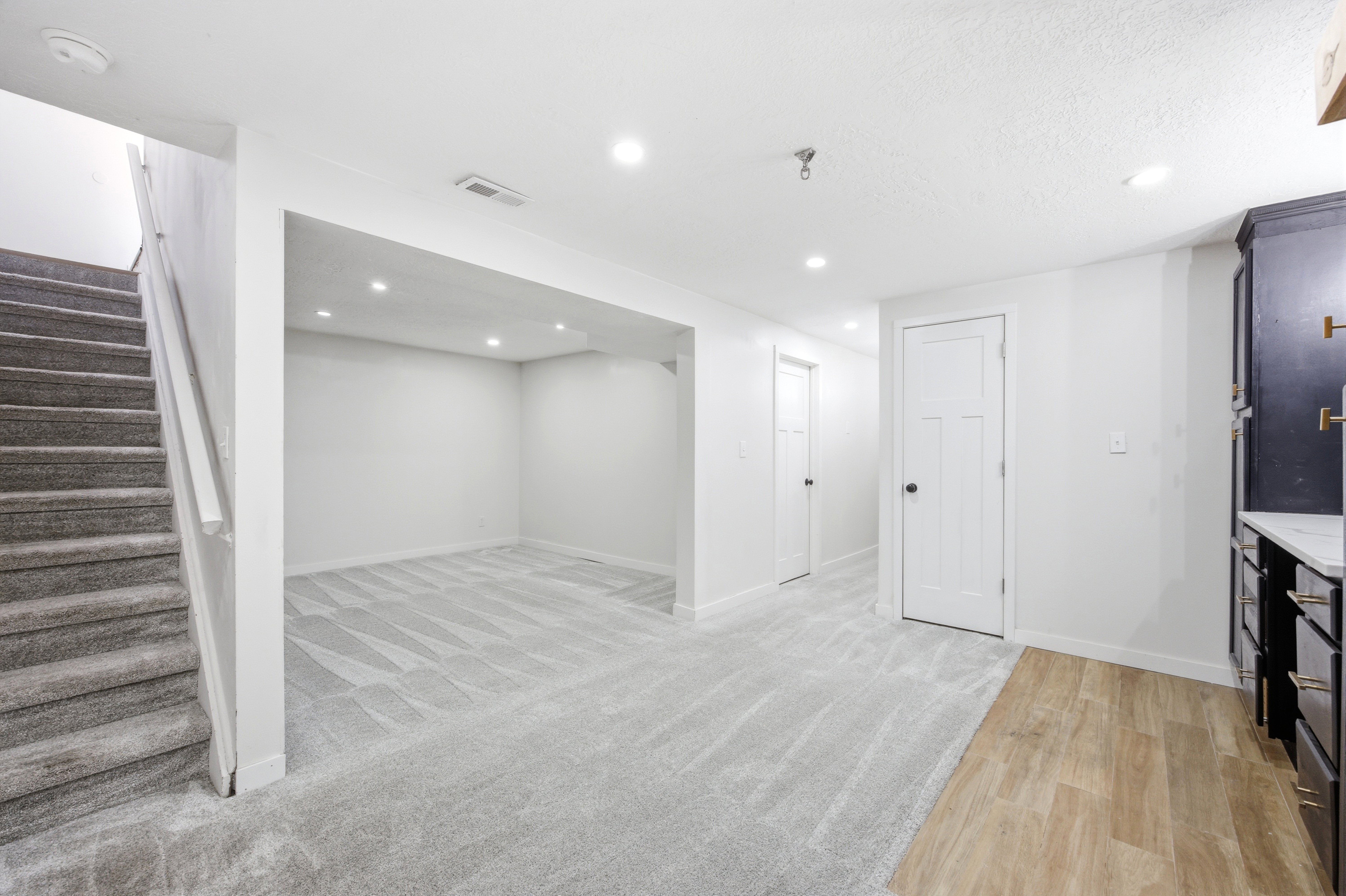 Versatile lower level featuring recessed lighting, plush carpet flooring, a dedicated stairwell, multiple white panel doors, and a built-in cabinetry unit with a light-toned countertop