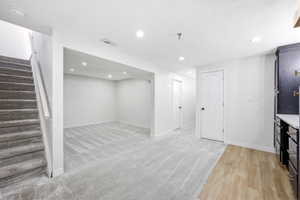 Versatile lower level featuring recessed lighting, plush carpet flooring, a dedicated stairwell, multiple white panel doors, and a built-in cabinetry unit with a light-toned countertop