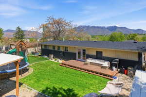 Back of property featuring a trampoline, an outdoor hangout area, a playground, a deck with mountain view, and french doors