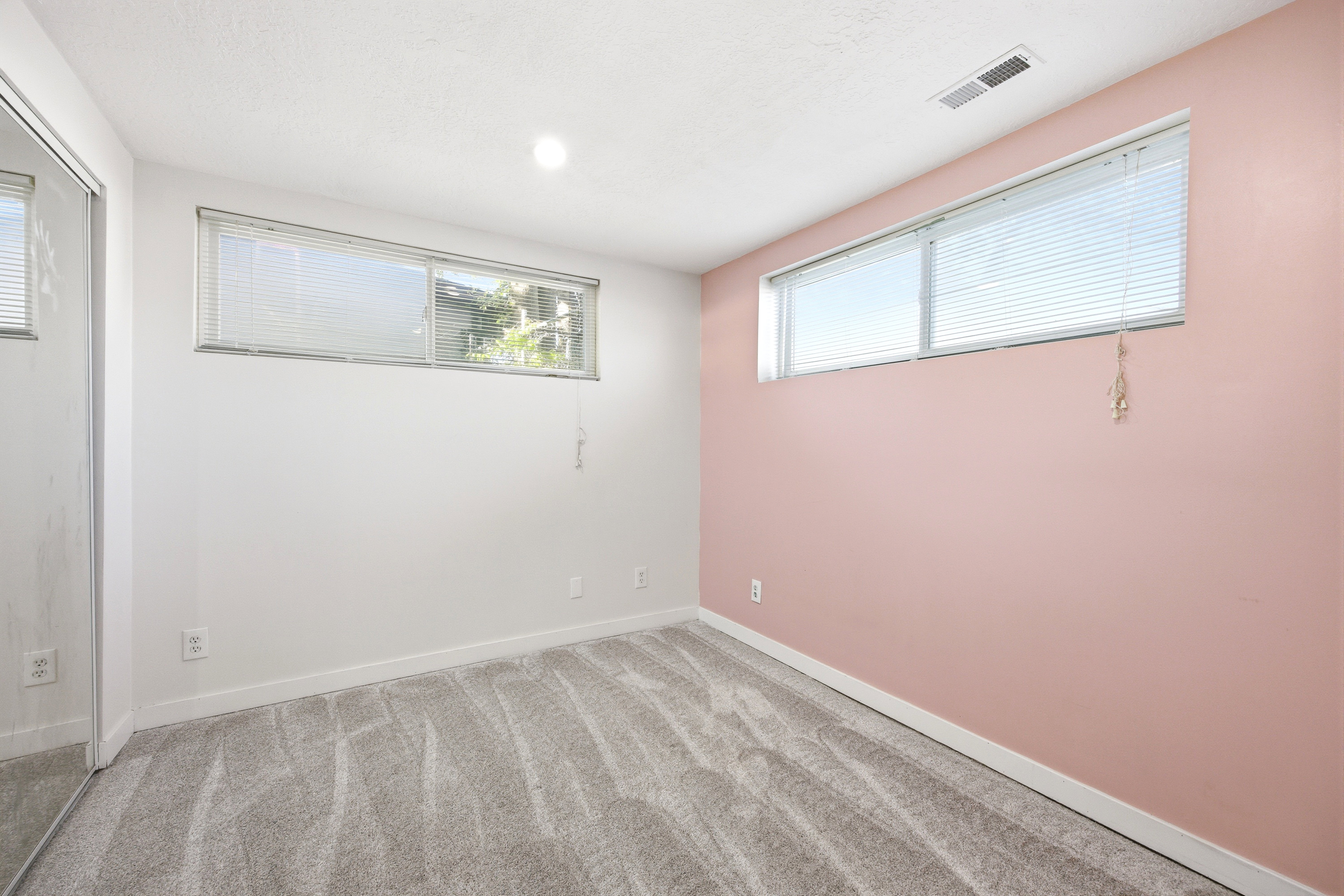 Carpeted interior space featuring a mirrored closet, two windows with blinds, a white ceiling with recessed lighting, and a neutral color palette