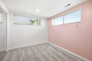 Carpeted interior space featuring a mirrored closet, two windows with blinds, a white ceiling with recessed lighting, and a neutral color palette
