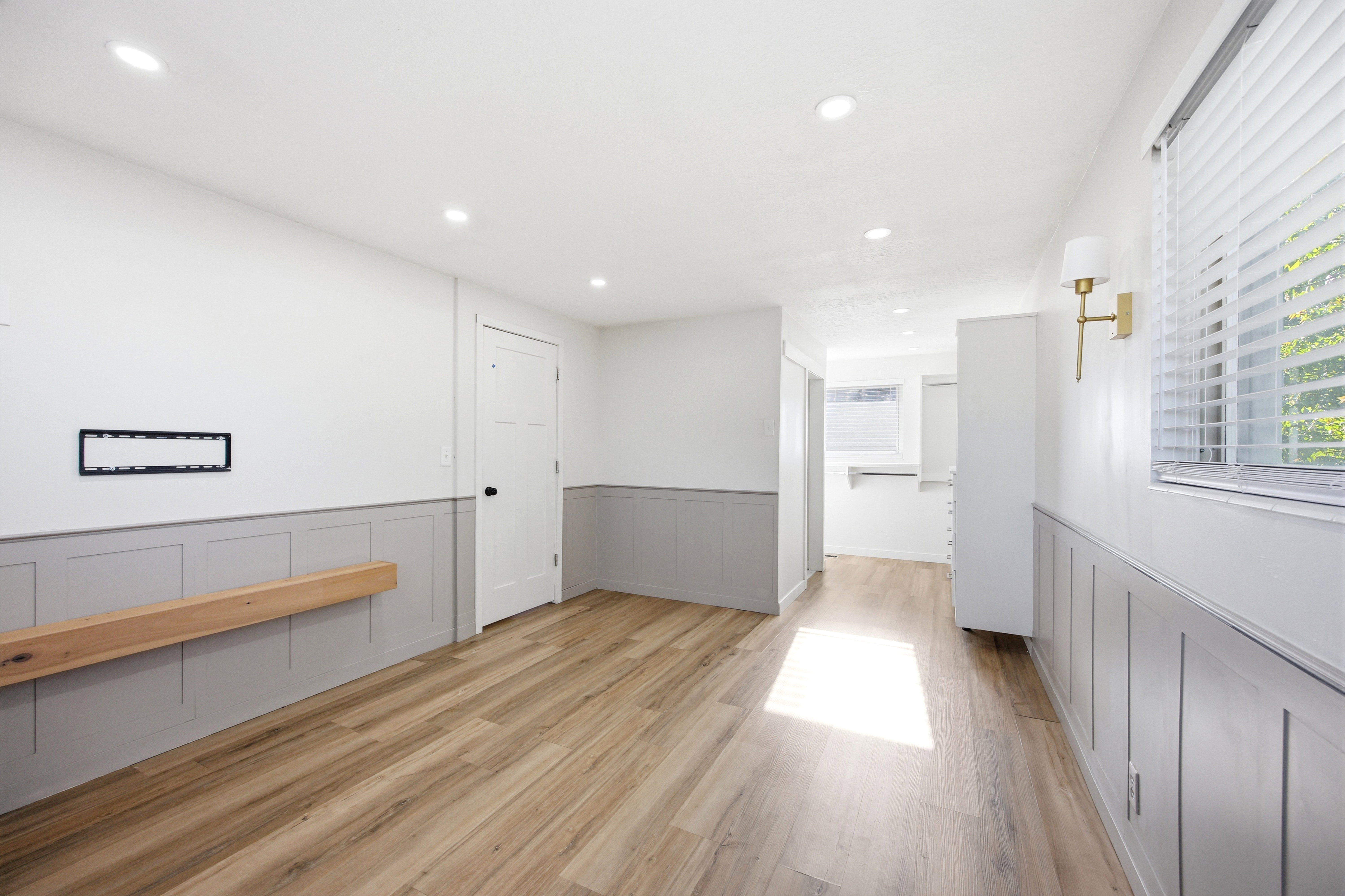Spacious room with wood-finish flooring, recessed lighting, and white walls featuring gray wainscoting