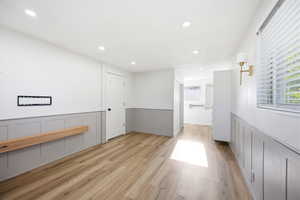 Spacious room with wood-finish flooring, recessed lighting, and white walls featuring gray wainscoting