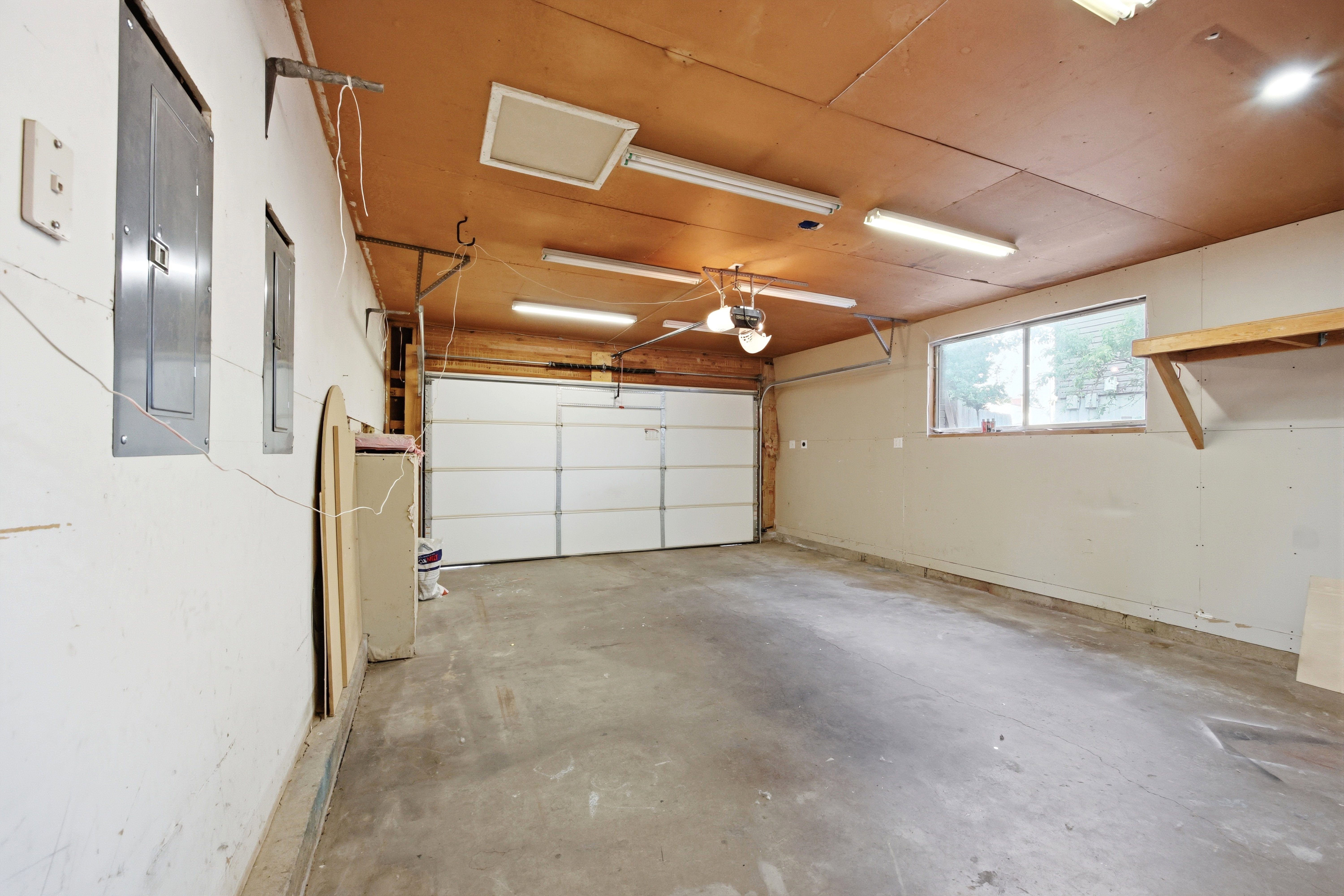 Spacious two-car garage featuring a concrete floor, an overhead garage door, built-in shelving, and a window for natural light
