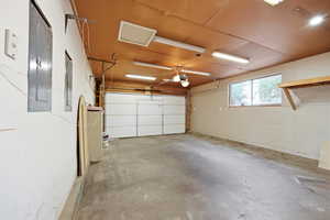 Spacious two-car garage featuring a concrete floor, an overhead garage door, built-in shelving, and a window for natural light