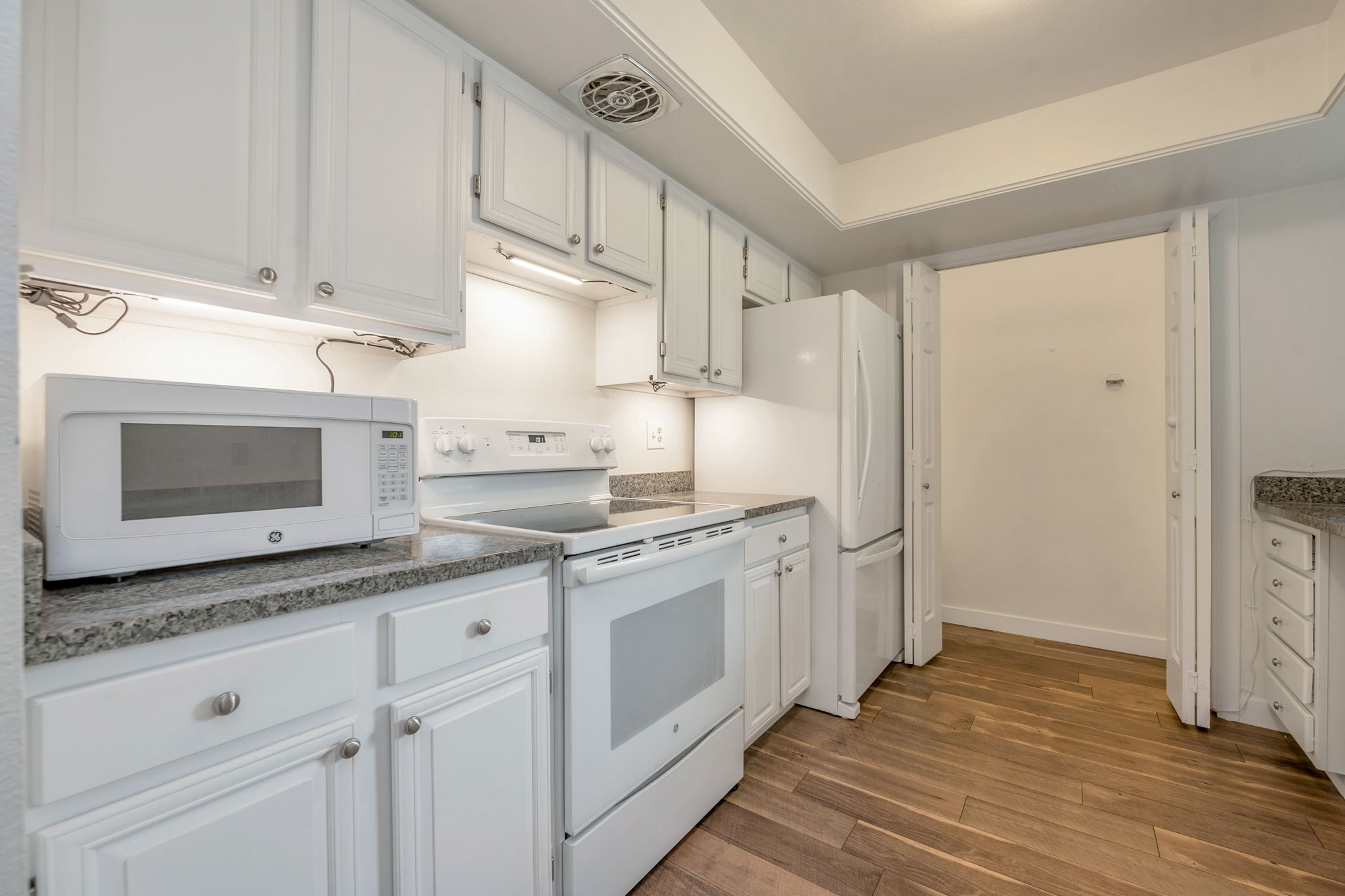 Kitchen featuring white appliances, white cabinetry, and laminate wood-style floors and pantry.