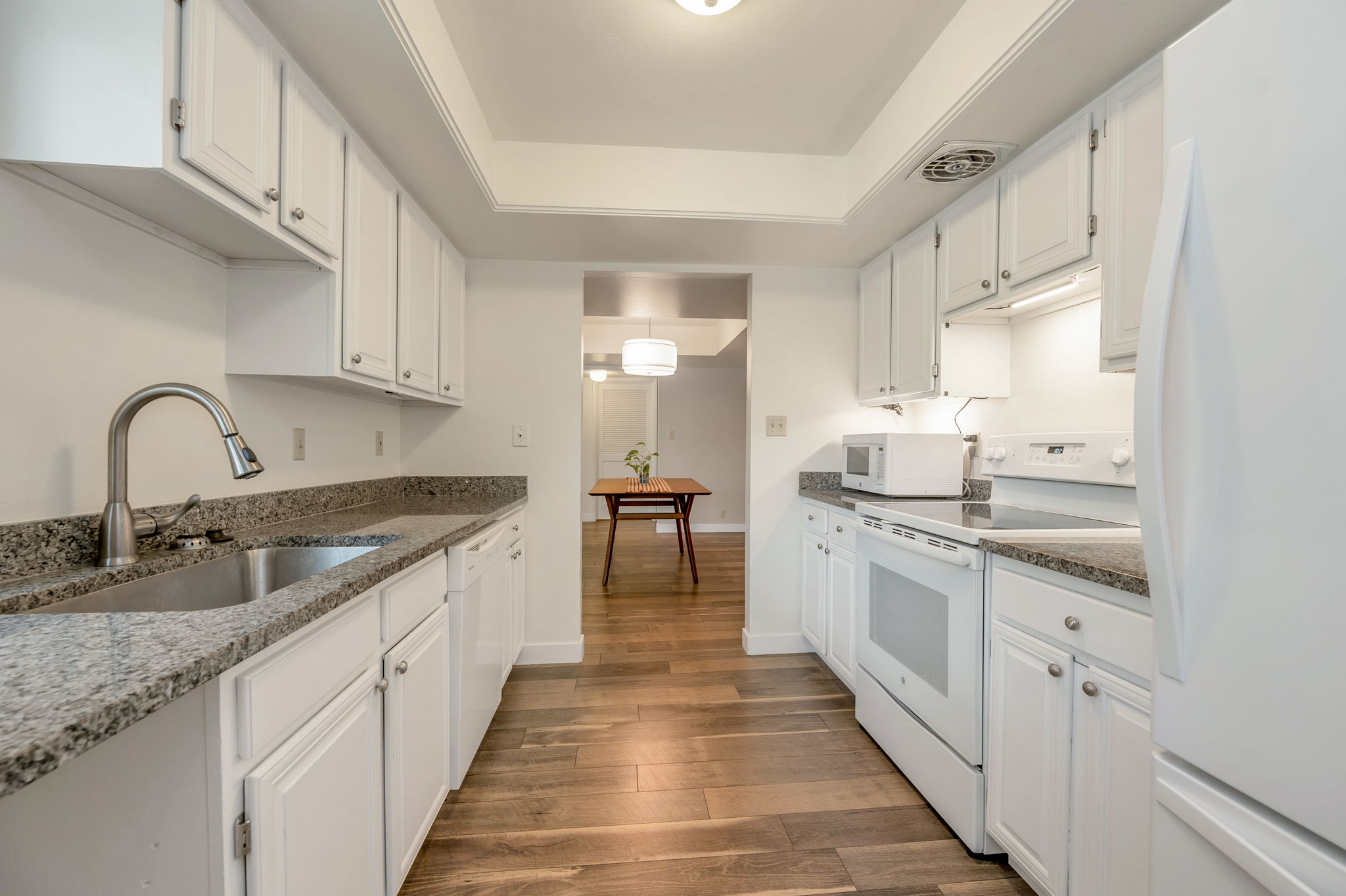 Kitchen featuring branite countertops, white cabinets, white appliances and laminate wood-style flooring.