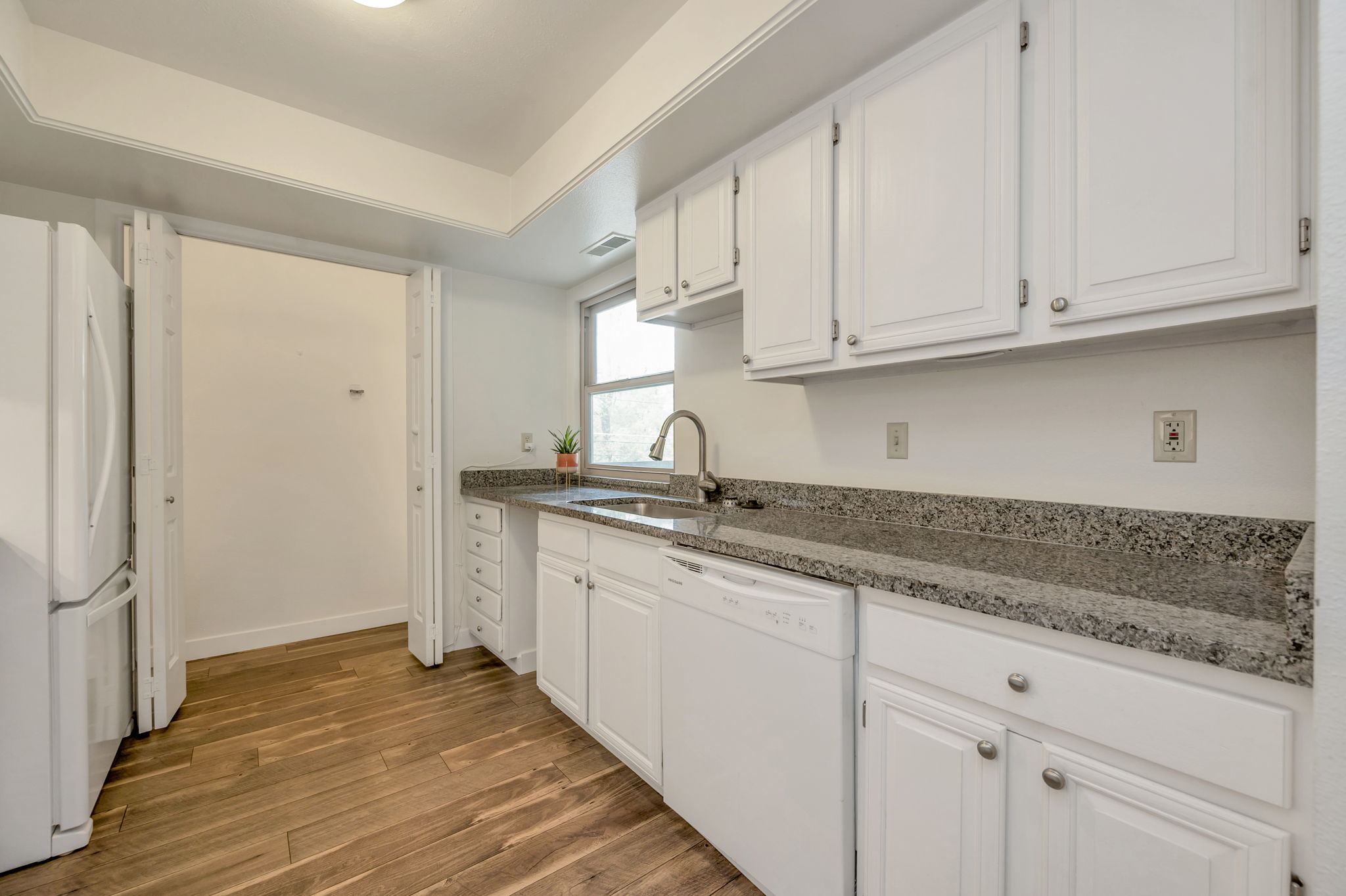 Kitchen featuring granite countertops, white cabinets, white appliances for a seemless clean look and laminate wood-style flooring.