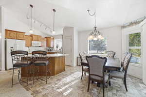 Kitchen and dining area featuring vaulted ceilings, light wood cabinetry, a center island with a light-toned countertop, and patterned tile flooring