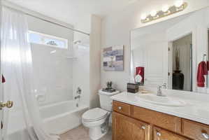 Bathroom featuring a combination bathtub and shower with white surround, a transom window, a vanity with wood-finish cabinetry, a white countertop, and an oval undermount sink