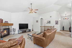 Living area featuring a stone-clad fireplace with a wood mantel, vaulted ceilings, and carpet flooring