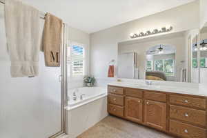 Bathroom featuring a soaking tub, glass-enclosed shower, dual vanity with wood cabinetry, and a large mirror with overhead lighting