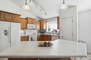 Kitchen featuring a peninsula with a light-toned countertop, wood cabinetry, vaulted ceilings, track lighting, and a window with horizontal blinds
