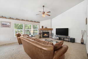 Living area featuring a corner stone fireplace with a wood mantle, vaulted ceiling, and ceiling fan