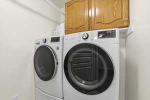 Laundry area featuring white front-loading appliances, upper wood-finish cabinetry, a built-in shelf, and light-colored walls