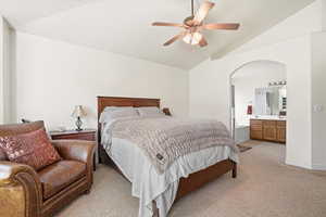 Spacious sleeping area with vaulted ceiling and ceiling fan, featuring an arched doorway leading to a private bath with a double vanity and built-in tub