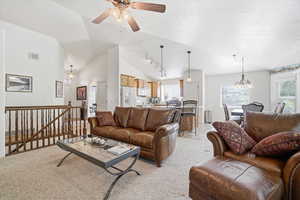 Spacious living area featuring vaulted ceilings, a ceiling fan, and carpet flooring