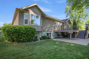 Rear view of property with stucco siding, a wooden deck, a yard, and a patio