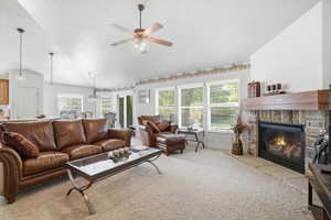 Living area featuring a stone fireplace with a wood-beam mantel, vaulted ceilings, and a ceiling fan