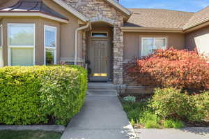 Property entrance with stone siding, stucco siding, and a shingled roof