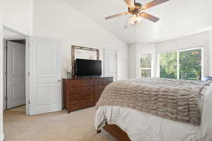 Vaulted ceiling bedroom featuring ample natural light from multiple windows, a ceiling fan, and light-toned carpeting