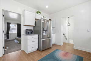 Kitchen with white cabinets, stainless steel fridge, and light wood-style flooring