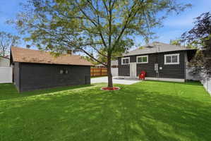 Rear view of property with a fenced backyard, an outdoor structure, a patio area, and a shingled roof