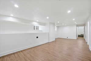 Finished basement featuring recessed lighting, light wood-style flooring, and a textured ceiling