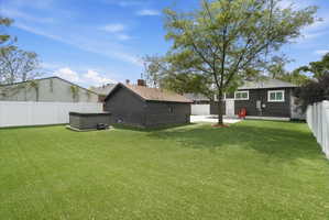 Rear view of house with a fenced backyard, a hot tub, and an outdoor structure